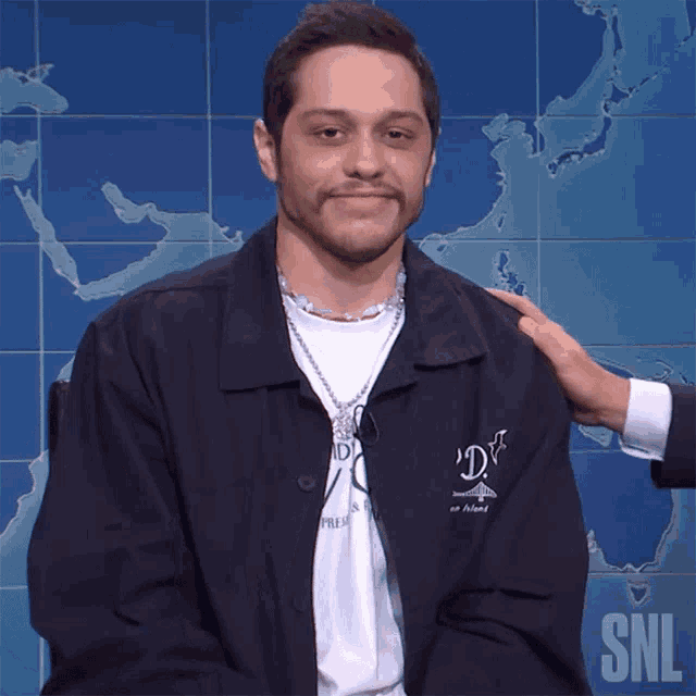 a man wearing a snl jacket is being patted on the shoulder