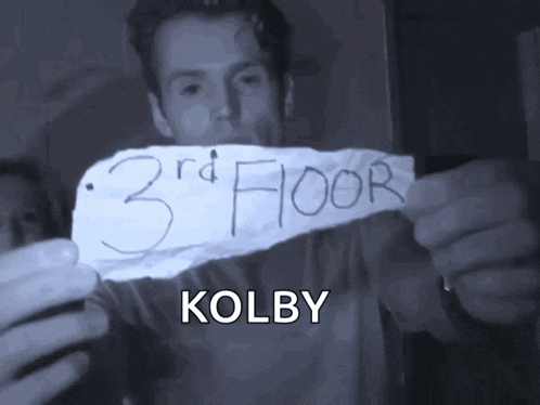 a man holds up a piece of paper that says kolby on it