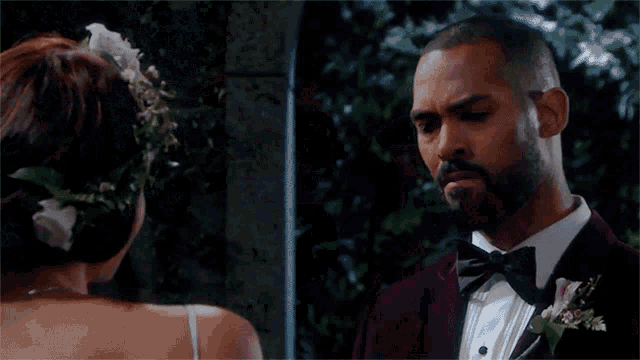 a man in a tuxedo stands next to a woman with a flower crown in her hair