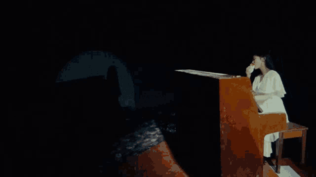 a woman in a white dress is playing a piano in a dark room .