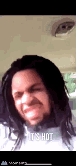 a man with dreadlocks is making a funny face with the words it 's hot below him