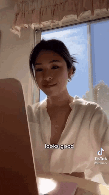 a woman in a white shirt is sitting in front of a laptop computer and says it looks good .