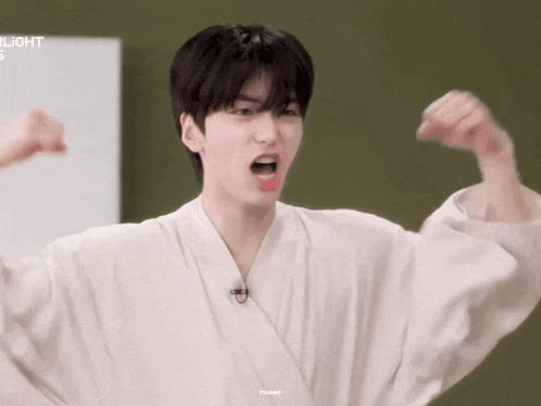 a young man wearing a white robe is flexing his muscles .