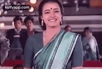 a woman in a saree is smiling at the camera while standing in front of a crowd .