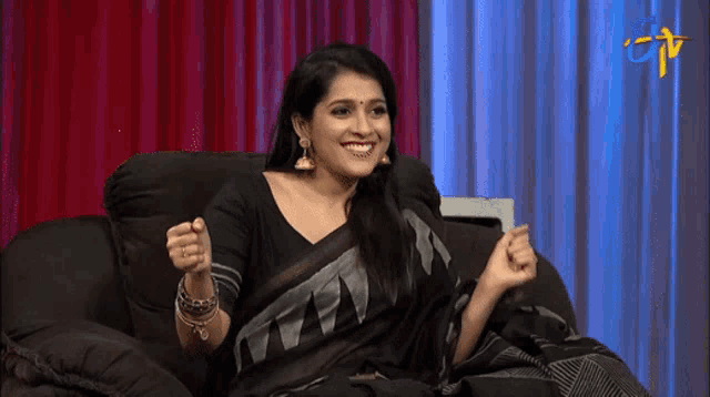 a woman in a black saree is sitting on a couch