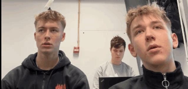 three young men are sitting in front of a fire alarm