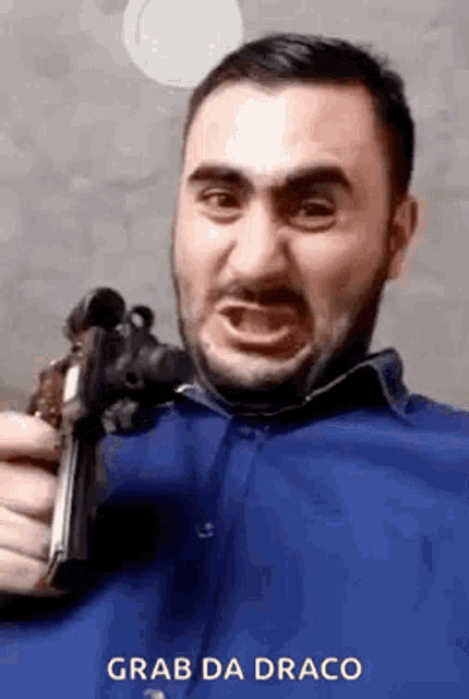 a man in a blue shirt is holding a gun in his hand and making a funny face .