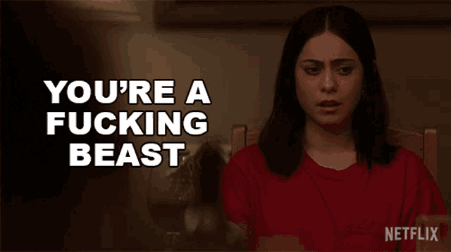 a woman in a red shirt is sitting at a table with the words " you 're a fucking beast " behind her
