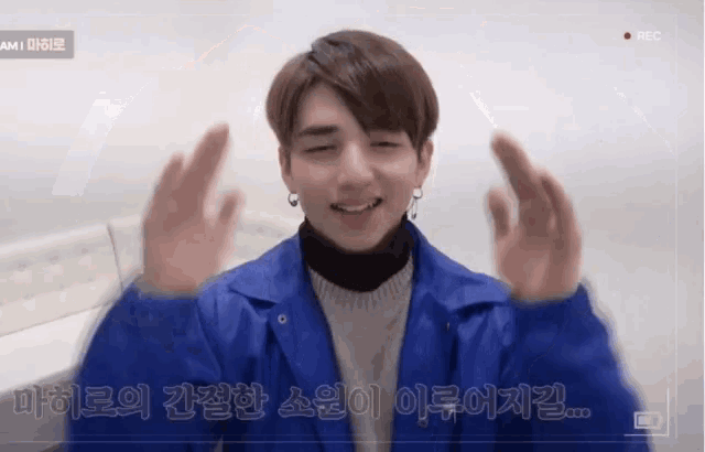 a young man in a blue jacket is smiling with his hands in the air