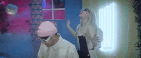 a man and a woman are dancing in a room . the woman is wearing a pink hat and sunglasses .