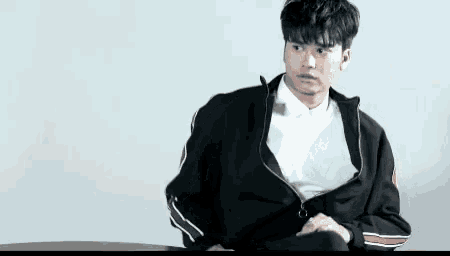 a young man in a black jacket sits at a table