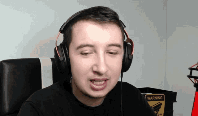 a man wearing headphones has a warning sign on the wall behind him