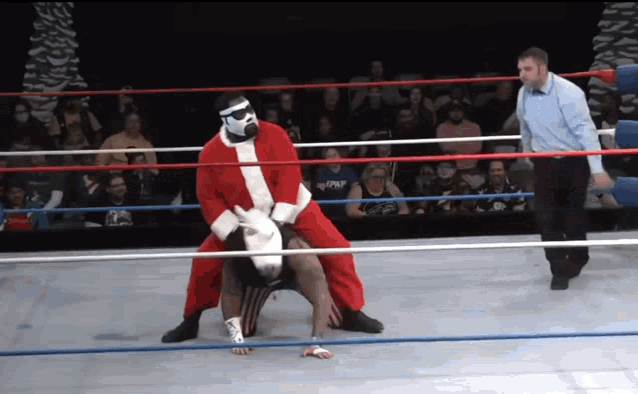 a wrestler in a santa suit is wrestling another wrestler in a ring