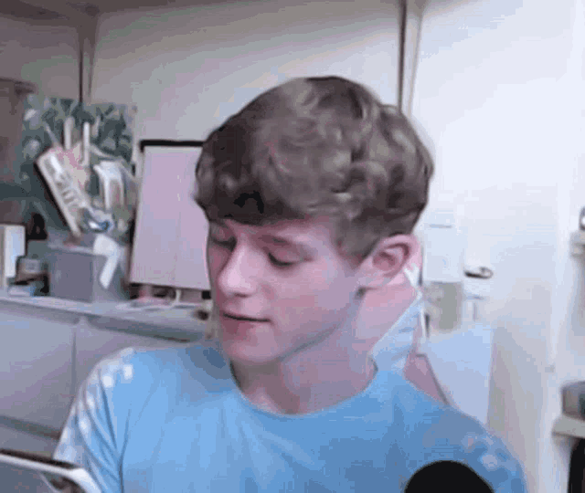 a young man in a blue shirt is sitting in front of a microphone in a room .