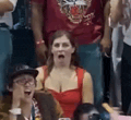 a woman in a red dress is sitting in a crowd of people with her mouth open .