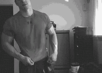 a black and white photo of a man in a t-shirt standing in a living room .