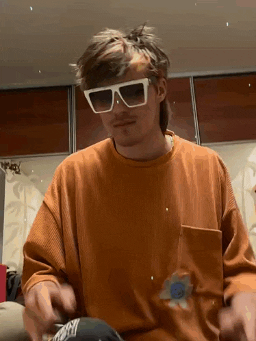 a man wearing sunglasses and an orange shirt is sitting on a couch in a room .