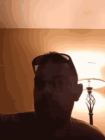 a man wearing sunglasses and a beard is standing in front of a lamp .