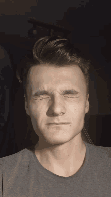 a man in a grey shirt makes a funny face with his eyes closed