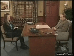 a man and a woman are sitting at a desk in an office talking to each other .