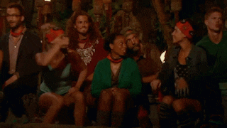 a group of people are sitting around a fire and a woman is dancing in the middle of the room .