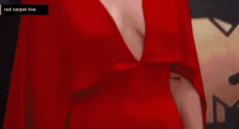 a woman in a red dress with a plunging neckline is walking down a red carpet .