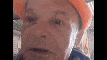 a close up of an older man wearing an orange hard hat .