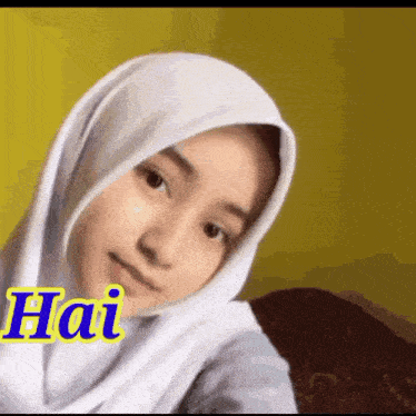 a girl wearing a white hijab is sitting on a couch and looking at the camera .
