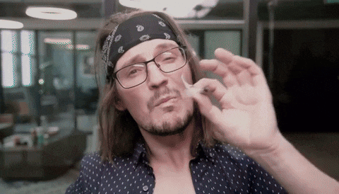 a man wearing glasses and a bandana holds a cigarette in his hand