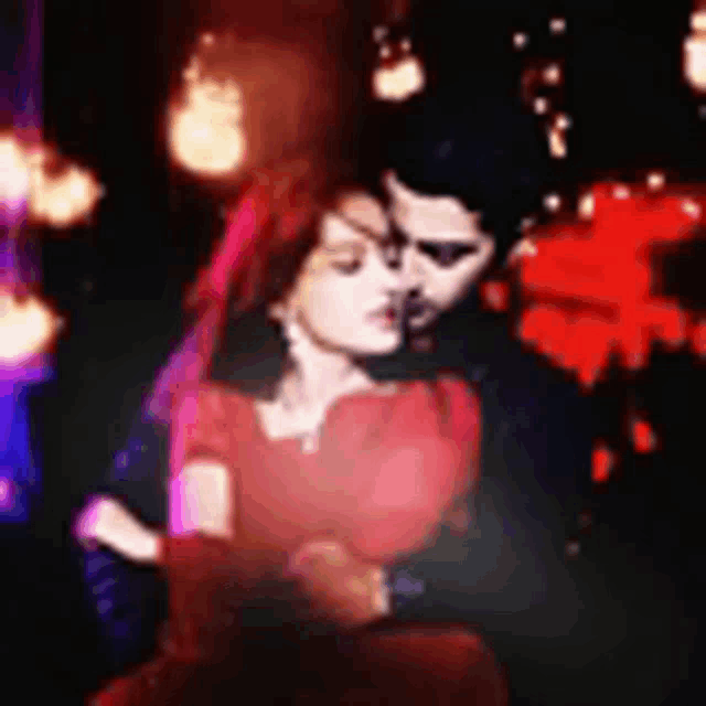 a man and woman are hugging each other in a dark room . the woman is wearing a red dress .