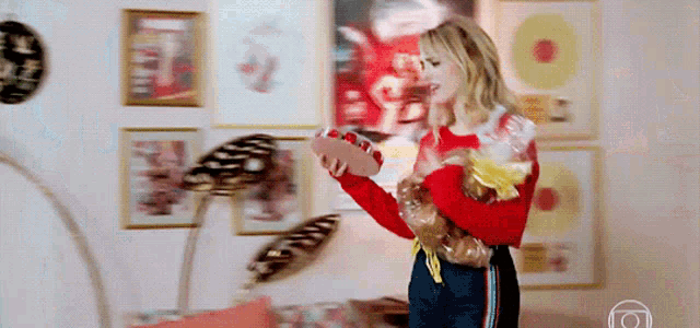 a woman in a red sweater is holding a bag of bread in front of a wall with pictures on it