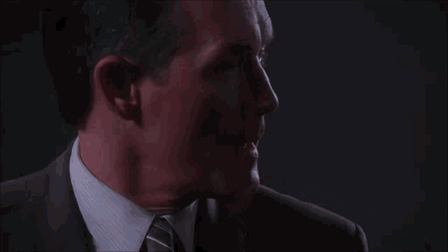 a man in a suit and tie looks at the camera with a serious look on his face
