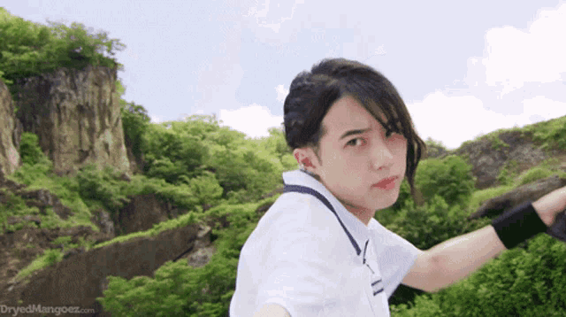 a man in a white shirt is standing in front of a mountain and the website dryedmangoez.com is visible