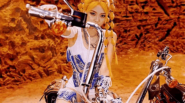 a woman is riding a motorcycle in the desert and pointing at the camera .