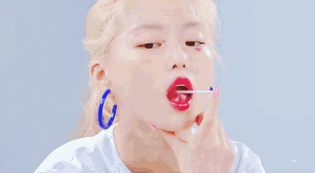 a close up of a woman applying lip gloss with a blue ring around her ear