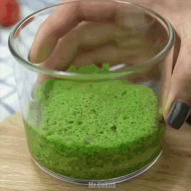 a person is holding a glass filled with green liquid and the word mr.cakes is on the bottom