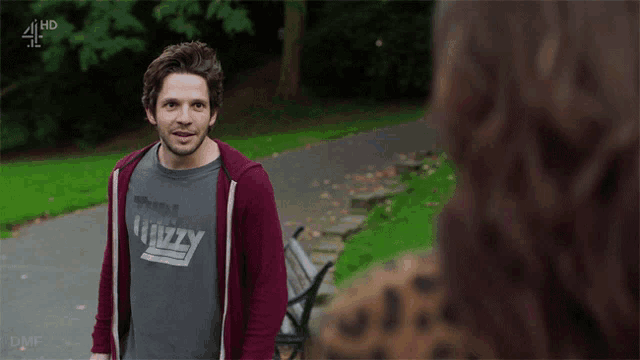 a man wearing a t-shirt that says ' think grizzly ' stands in a park