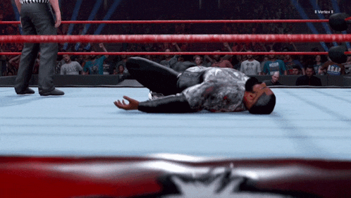 a man is laying on the floor in a wrestling ring with a referee standing behind him