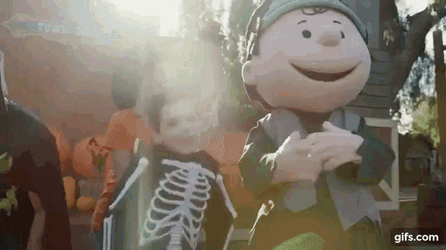 a boy in a skeleton costume is standing next to a stuffed peanuts character .