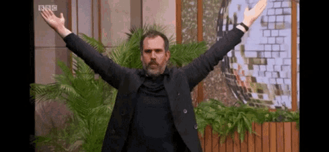a man in a black suit is standing with his arms outstretched in front of a disco ball .