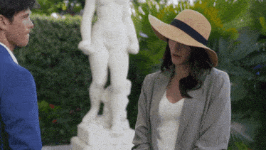 a woman in a hat stands in front of a statue of a woman