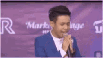 a man in a blue suit is singing into a microphone in front of a purple background .