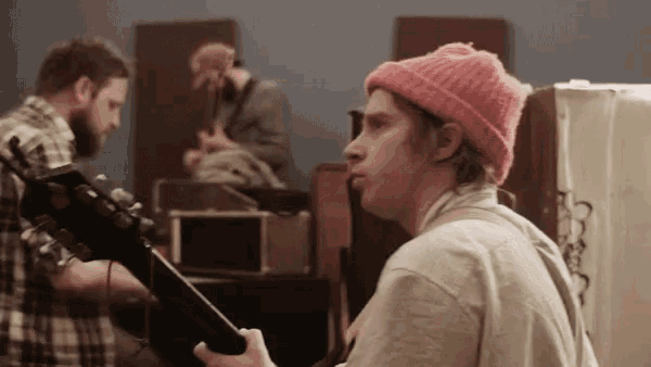 a man in a pink beanie is holding a guitar
