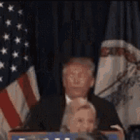 a woman in a plaid shirt is being held by a man in a suit in front of an american flag .