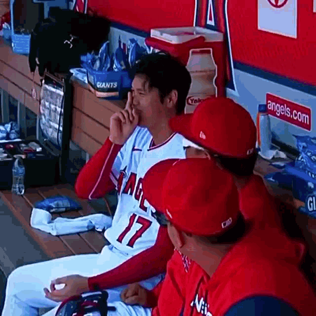 a baseball player wearing a number 17 jersey is sitting in a dugout with his teammates .