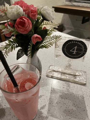 a glass of pink liquid sits on a table next to a table number four