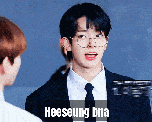 a young man wearing glasses and a suit has the word heeseung on the bottom right