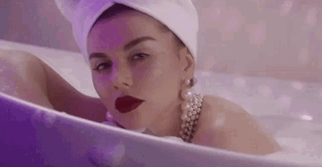 a woman with a towel wrapped around her head is laying in a bathtub .