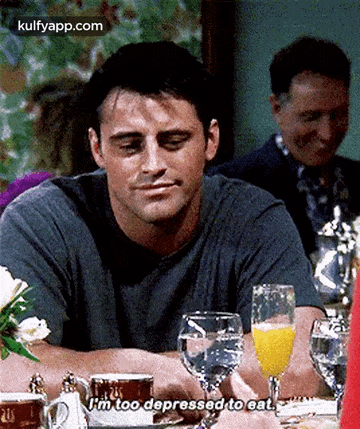 a man is sitting at a table with a glass of water and a glass of orange juice and talking .