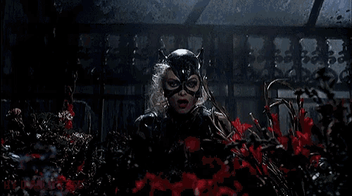 a woman in a black catsuit is screaming in a garden